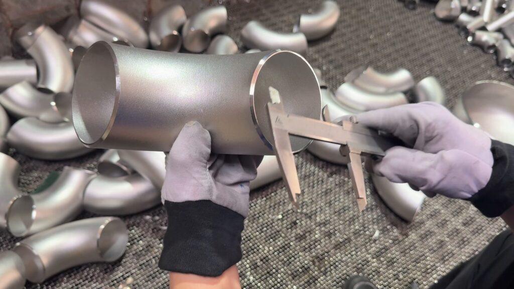 Inspector measuring a stainless steel butt-weld elbow with a vernier caliper